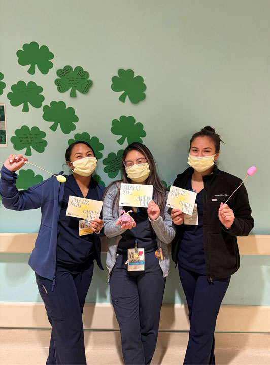 Three nurses standing and each holding “Thank You Child Life” cards