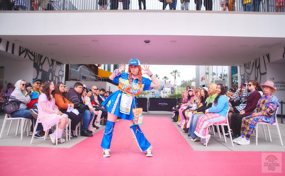 A fashion model dressed in mostly blue clothing with blue hat and red, pigtails poses during Kawaii Fashion Show