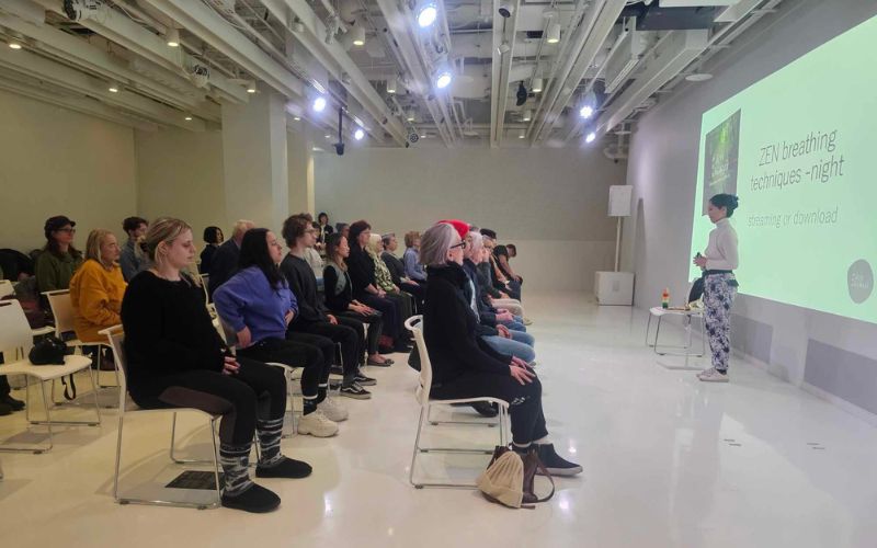 Instructor Yuki Shiina in front of a projector screen, teaching Zen Kokyū to a group of students sitting on chairs