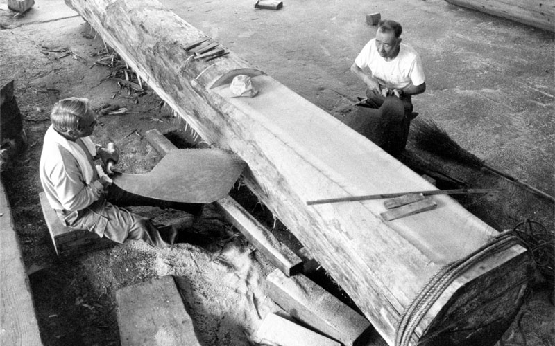 A black and white photo of two Japanese carpenters sawing a log