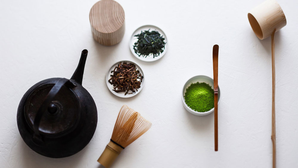 A teapot, plates with tea leaves, a teacup with green tea powder and wooden spoons