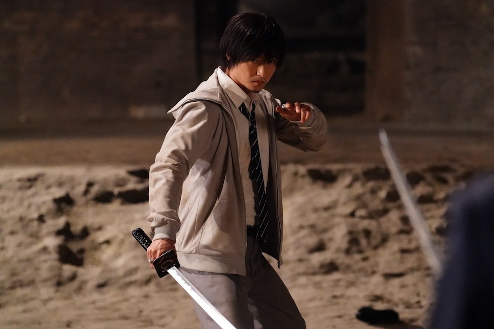 Film still from "Under Ninja." Protagonist, Kuro Kumogakure (Kento Yamazaki) holds a Japanese sword against an unknown assailant that also had a sword outside in a dusty area.