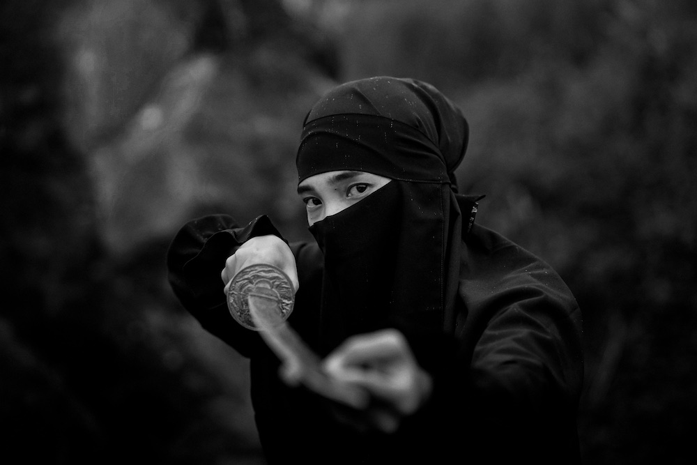 A man in ninja outfit holding a sword, black and white.