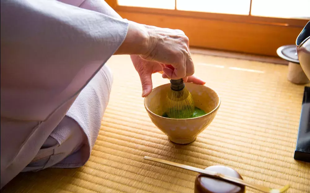 A lady in a kimono, whisking gree tea in a cup