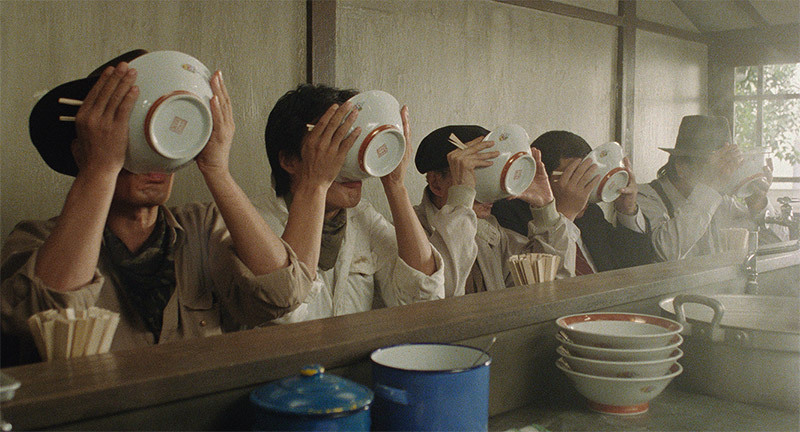 Several people at a counter holding bowls to their faces, appearing to drink or slurp from them, likely from the film Tampopo. 